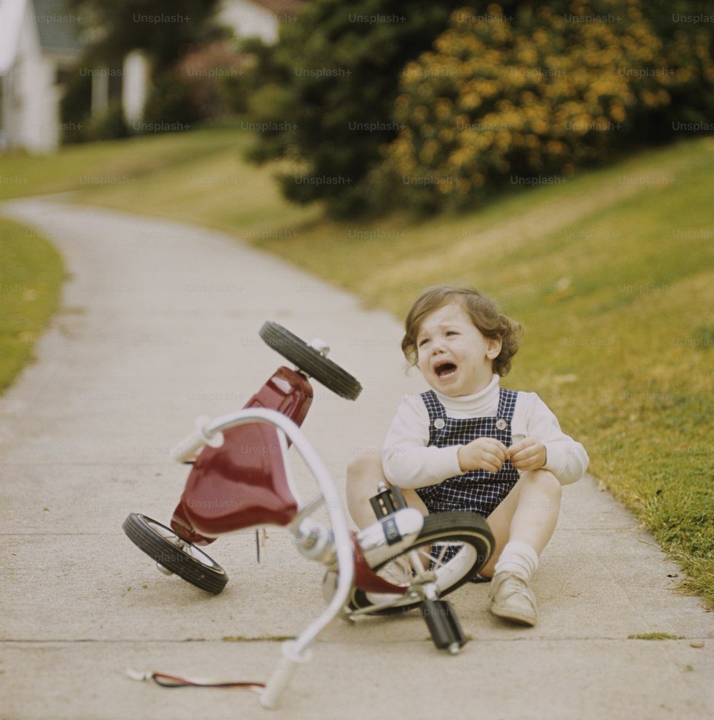 赤い自転車の隣の地面に座っている小さな女の子