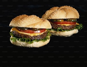 two cheeseburgers with lettuce and tomato on a black background