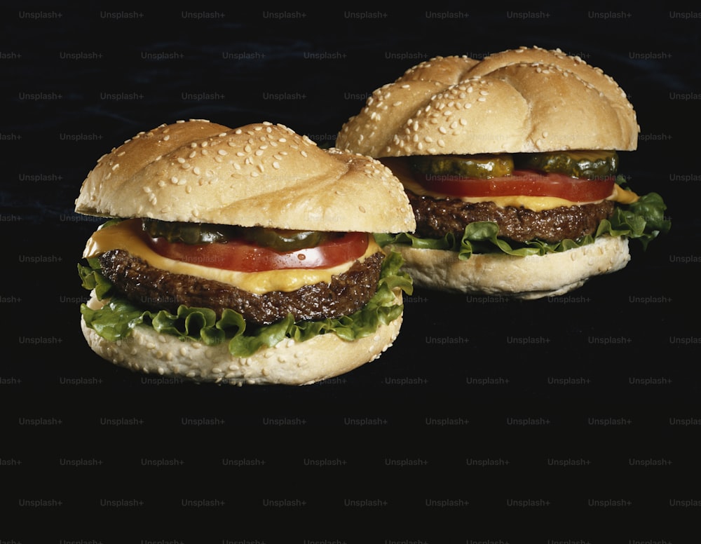 Dos hamburguesas con queso con lechuga y tomate sobre fondo negro