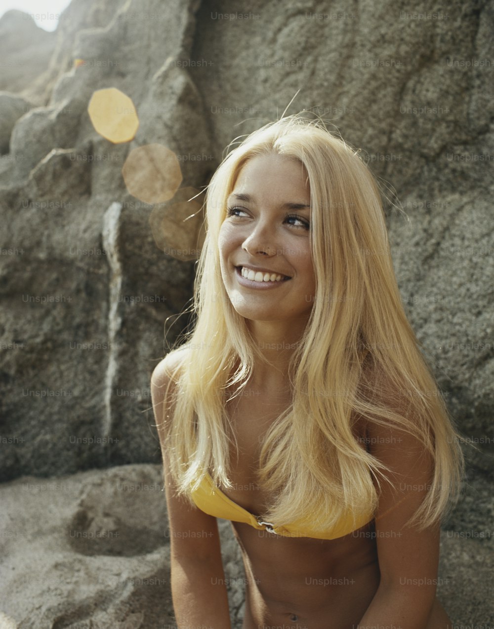 a woman in a yellow bikini sitting on a rock