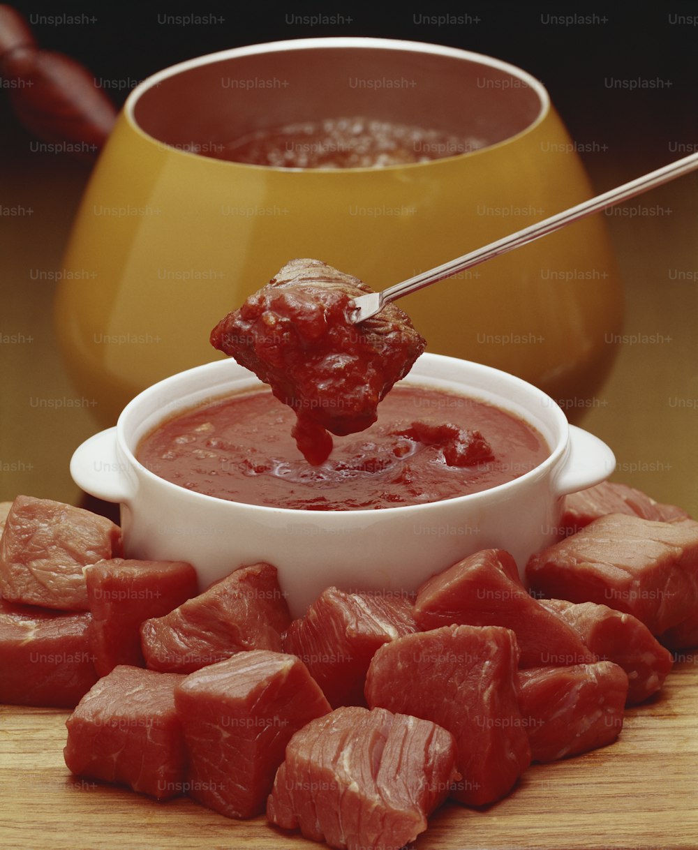 a bowl of red sauce with cubed meat on a cutting board