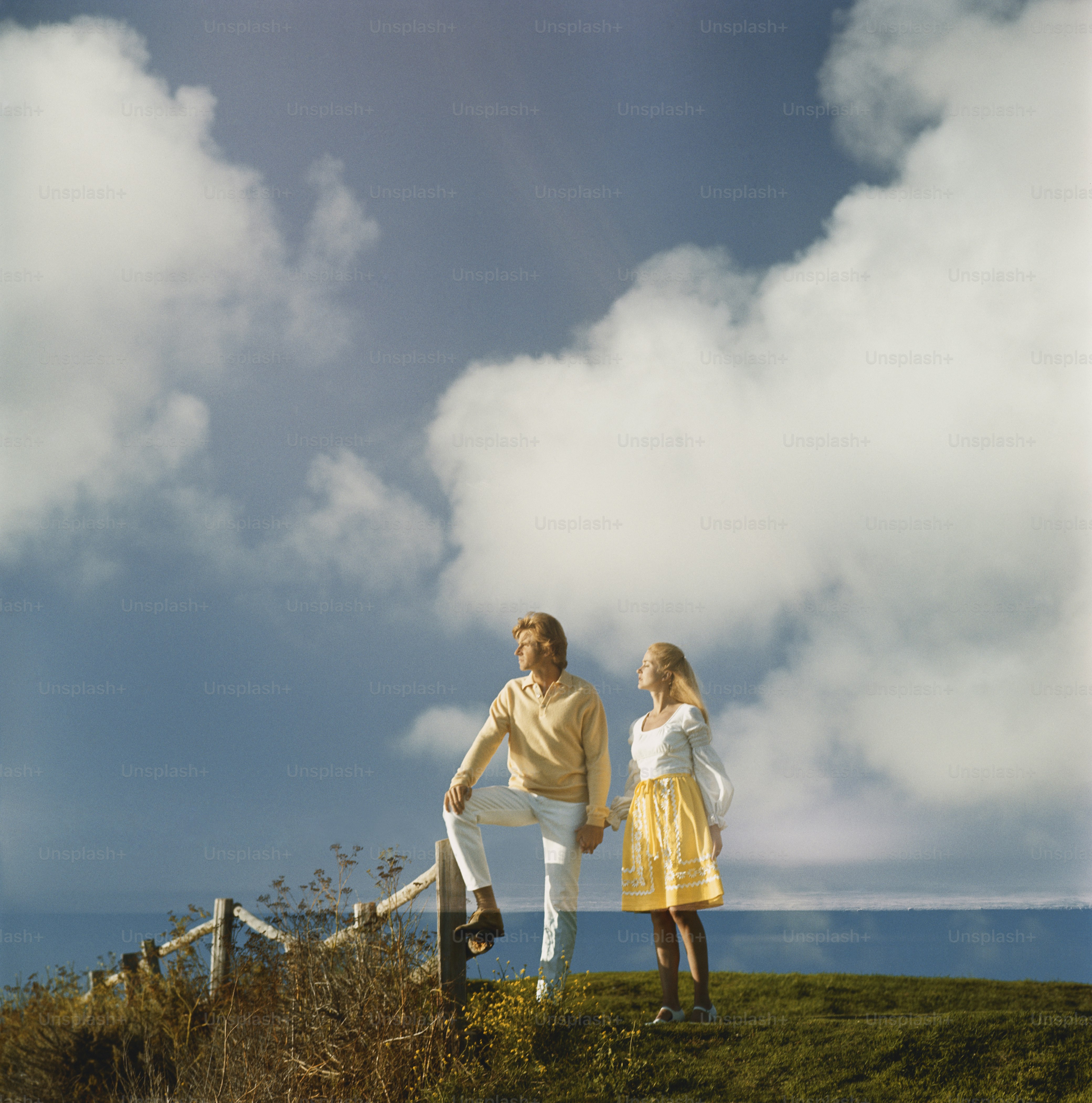 A man and a woman standing on top of a grass covered hill photo ...