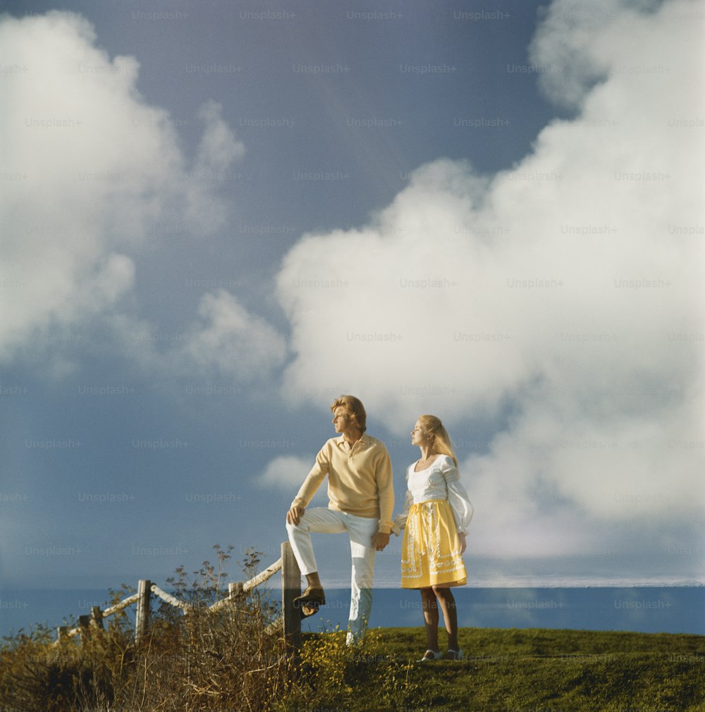 a man and a woman standing on top of a grass covered hill