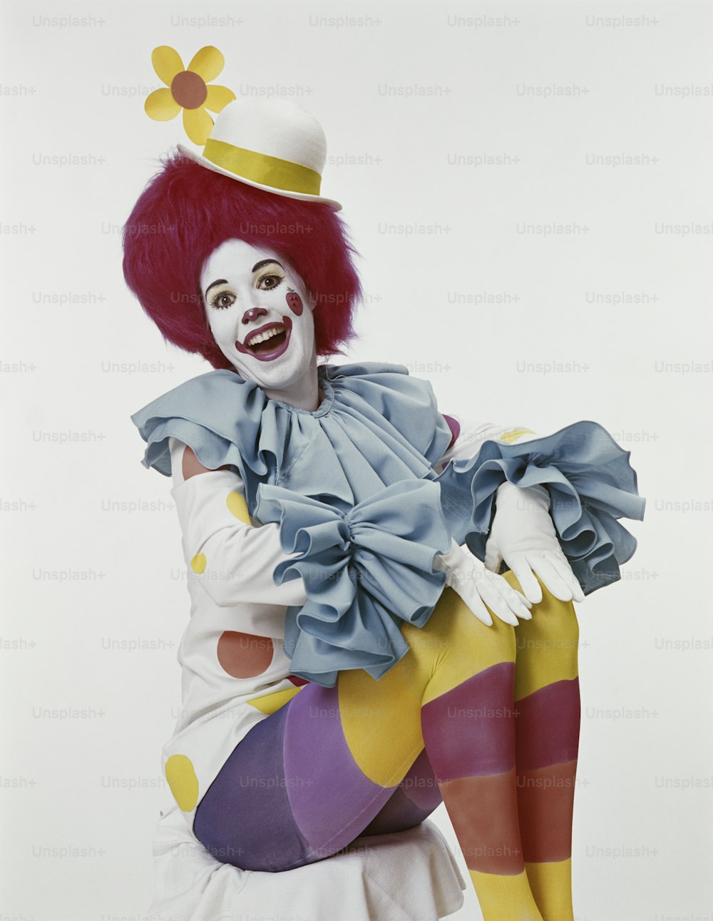 a clown sitting on the ground with a hat on