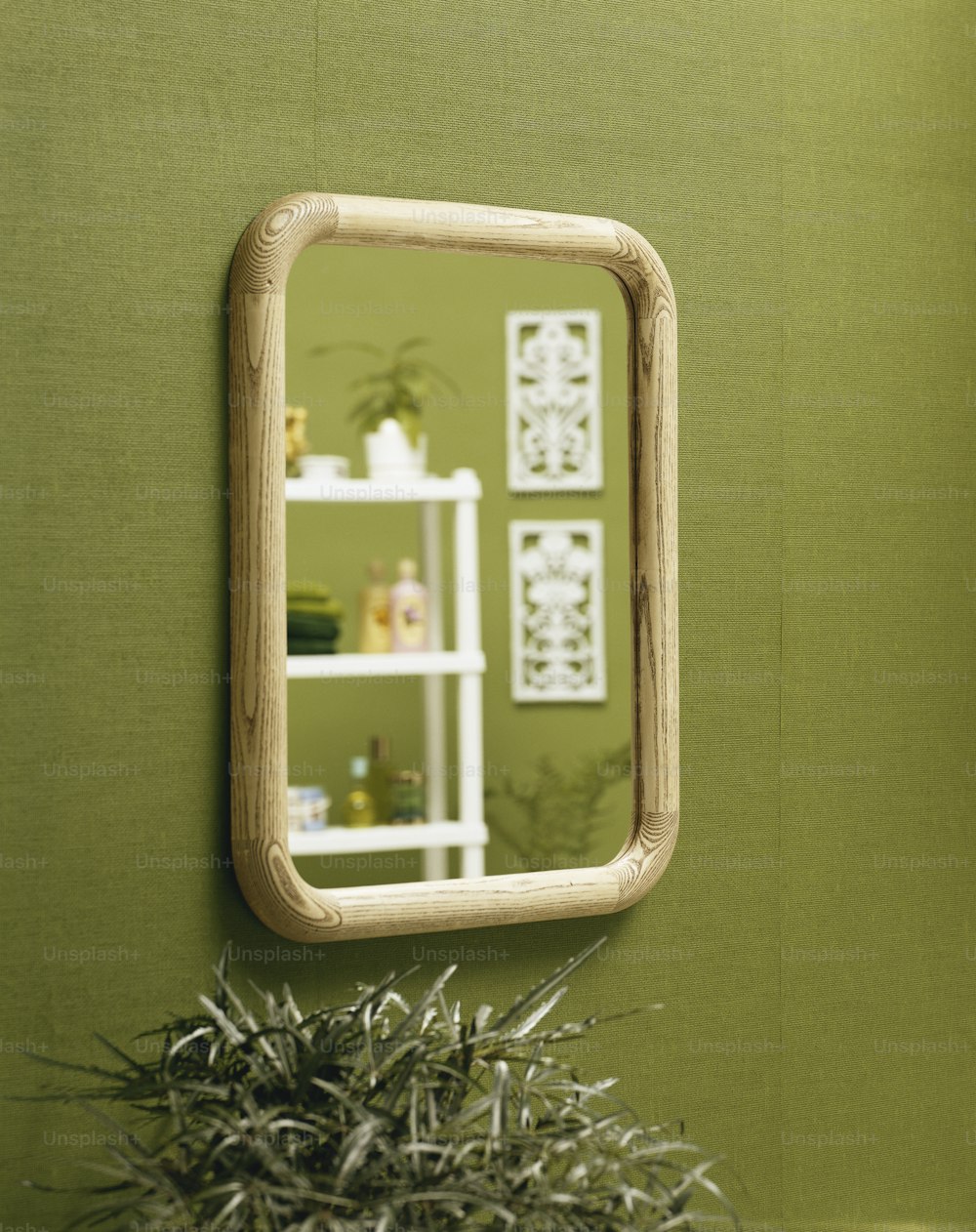 a mirror hanging on a green wall next to a potted plant