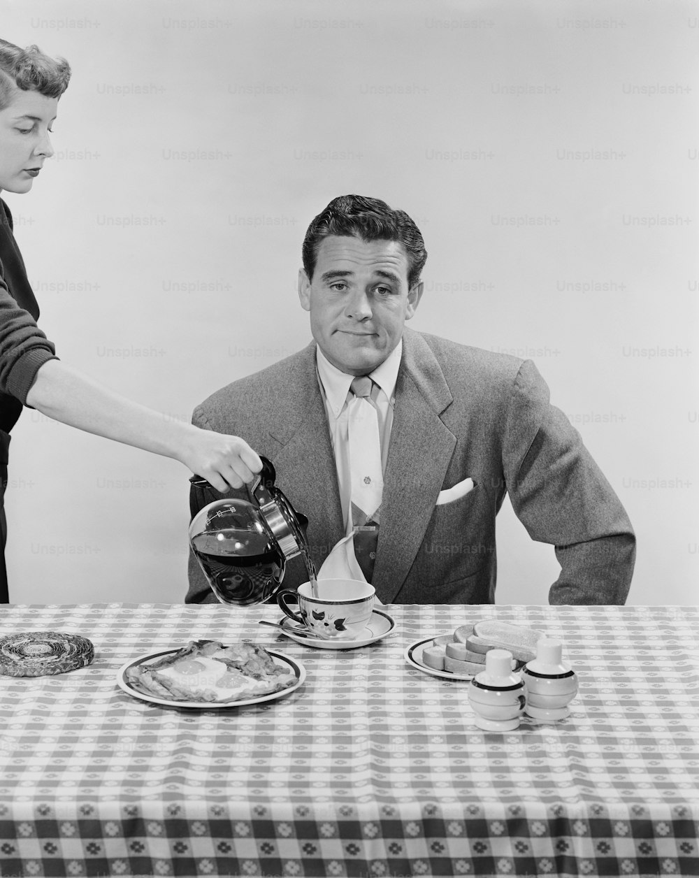 Una foto in bianco e nero di un uomo che versa il tè a un tavolo
