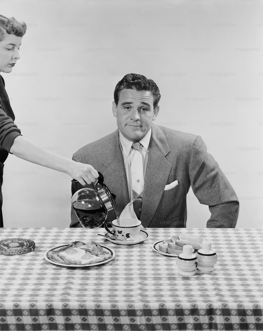 a black and white photo of a man pouring tea at a table