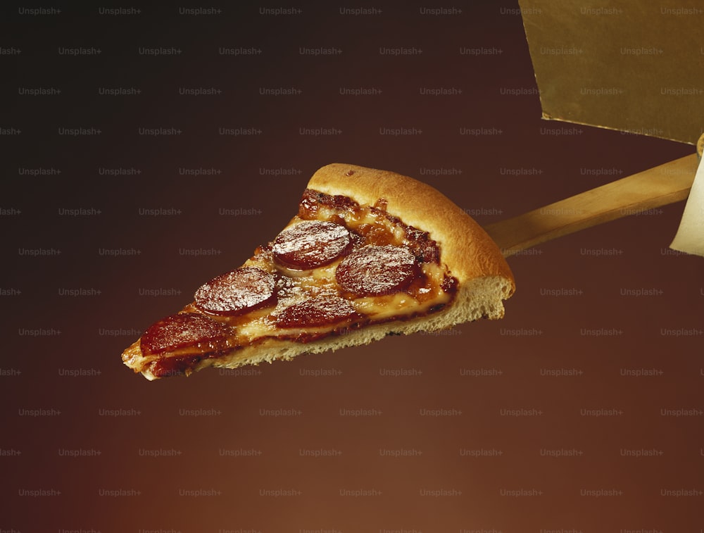 ein Stück Peperoni-Pizza, das von einem Holzspatel gehalten wird