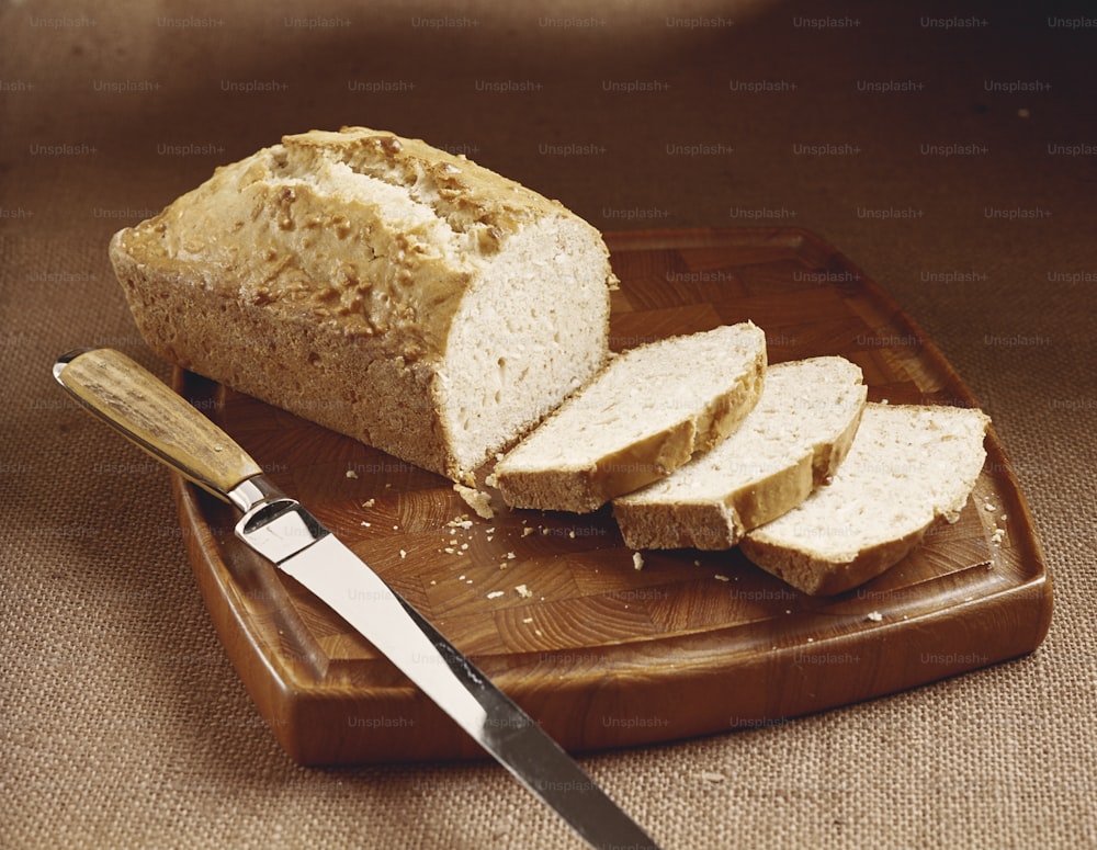 Una barra de pan sentada encima de una tabla de cortar junto a un cuchillo
