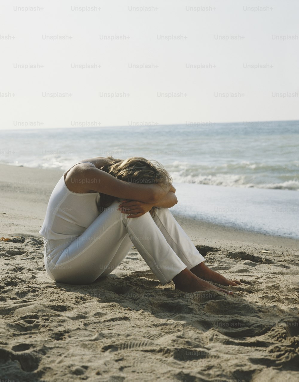 a woman sitting on the beach with her head in her hands