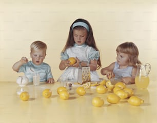 three little girls sitting at a table with lemons