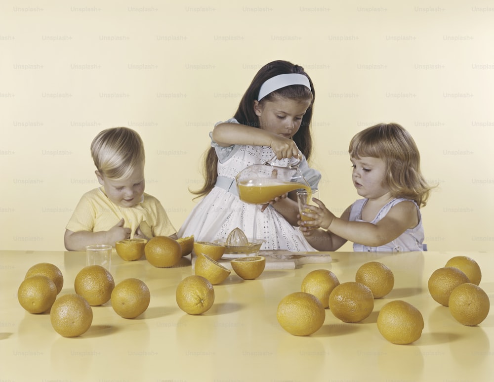 a group of young children standing around a table filled with oranges