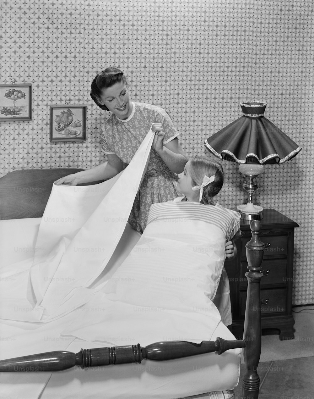 a woman helping a child put a sheet on a bed