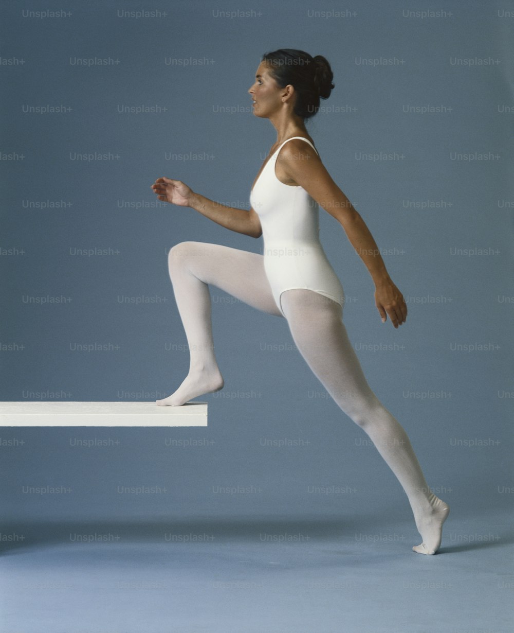 a woman in a white leotard jumping over a ledge
