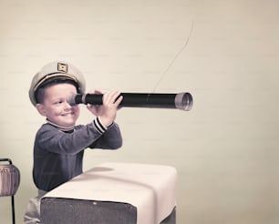 Ein kleiner Junge, der einen Hut trägt und ein Teleskop hält