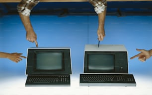 two hands pointing at a computer monitor and keyboard