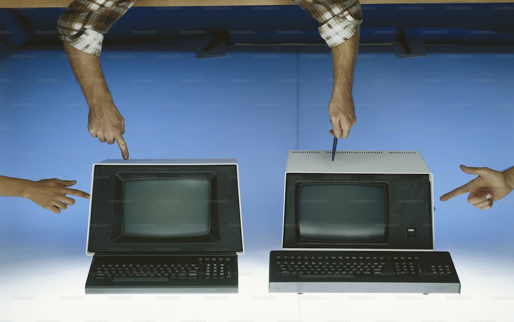 two hands pointing at a computer monitor and keyboard