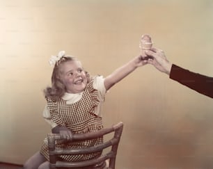 Una niña sentada en una silla sosteniendo una rosquilla
