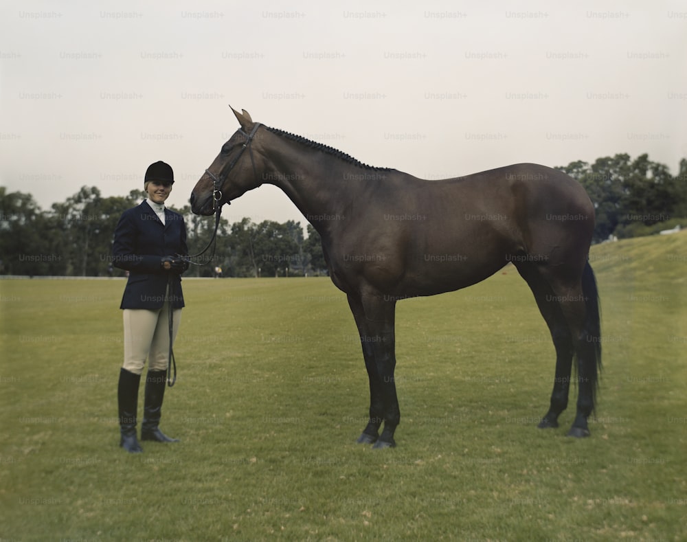 a woman standing next to a brown horse on a lush green field