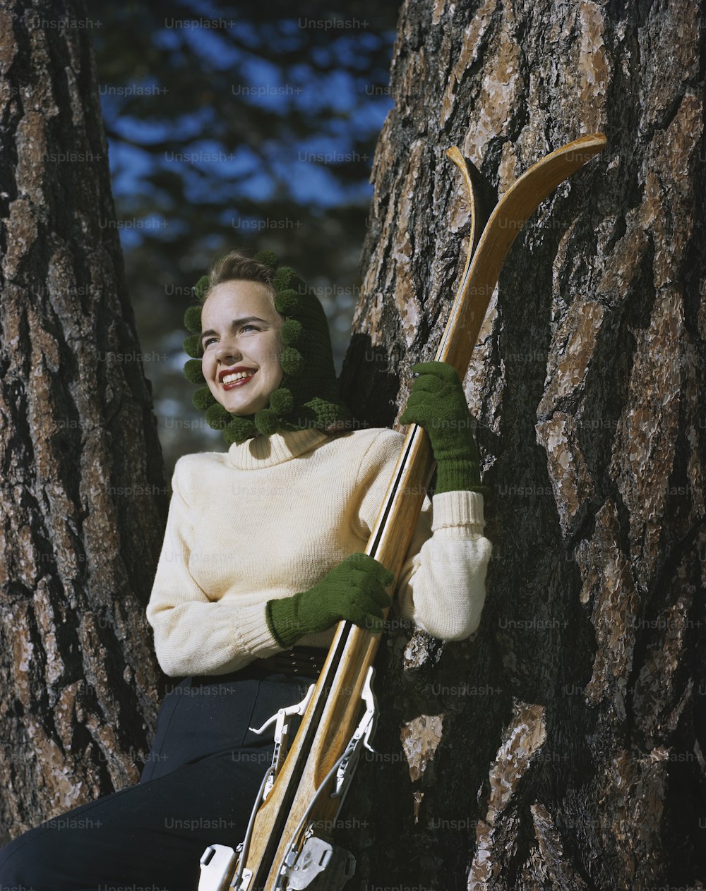 스키 한 켤레를 들고 나무에 앉아 있는 여자