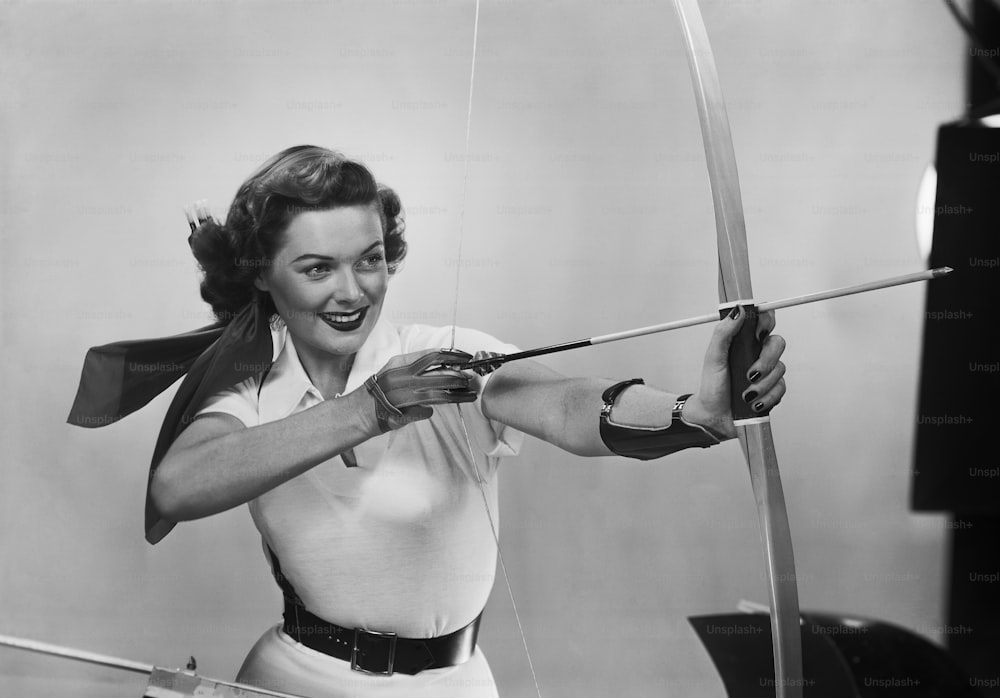 a black and white photo of a woman holding a bow and arrow