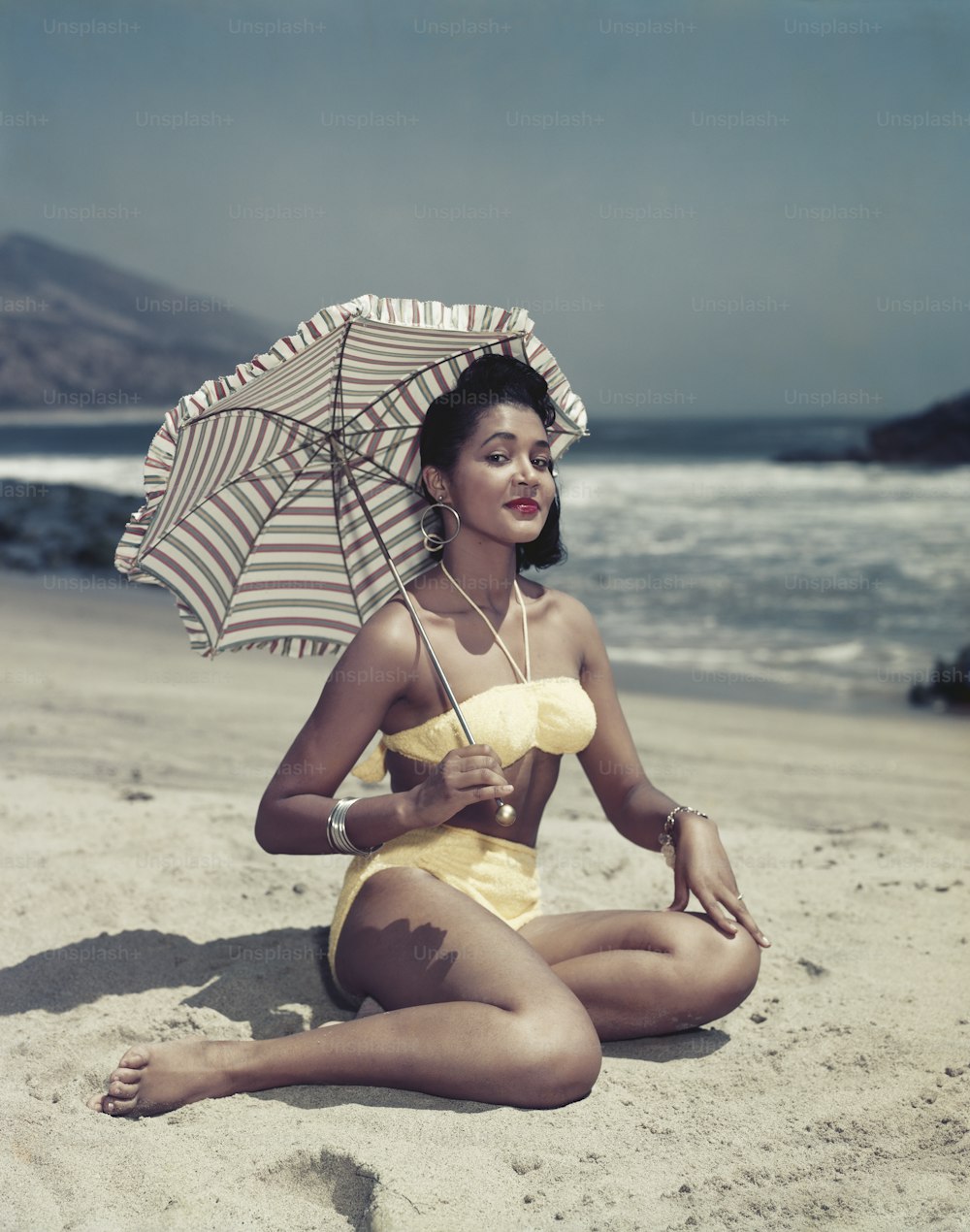 a woman sitting on the beach with an umbrella