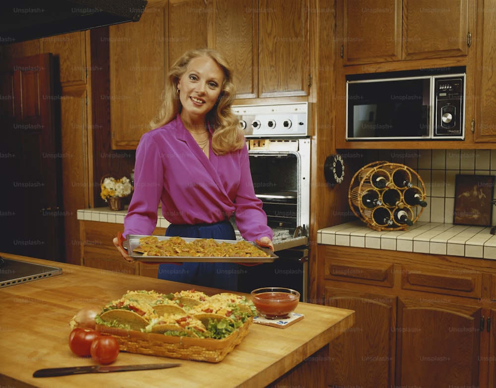 a woman holding a tray of food in a kitchen