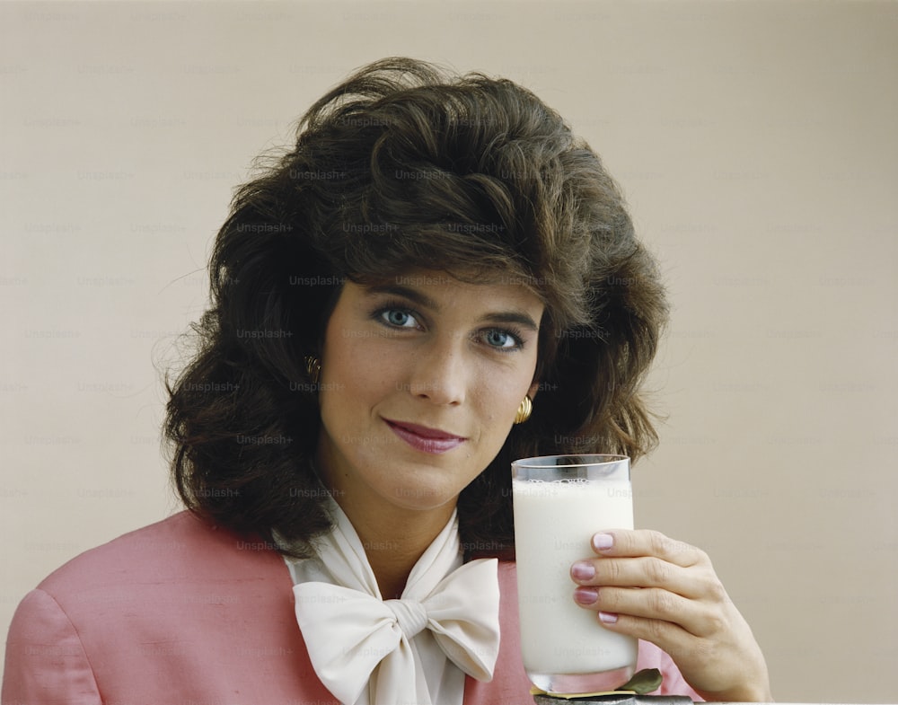Una mujer con una chaqueta rosa sosteniendo un vaso de leche