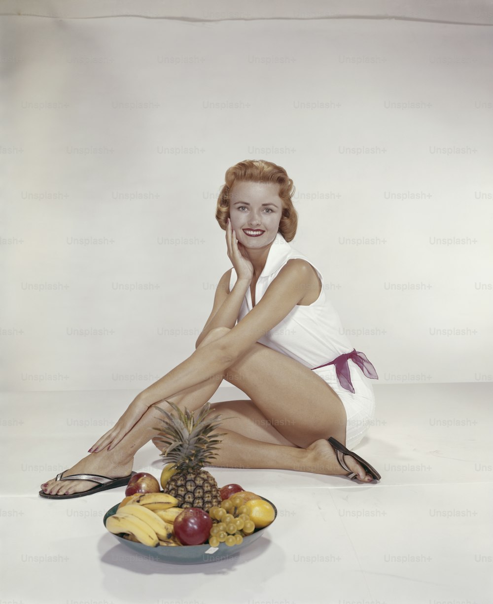 a woman sitting on the ground next to a plate of fruit
