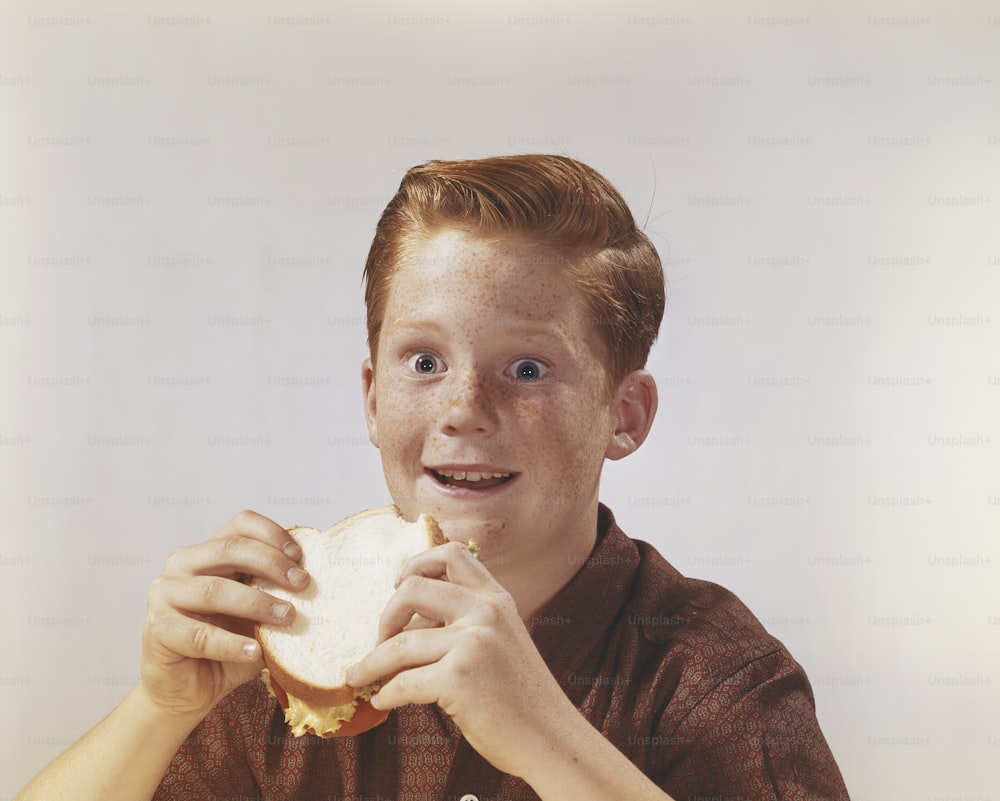 a young boy eating a sandwich with a smile on his face