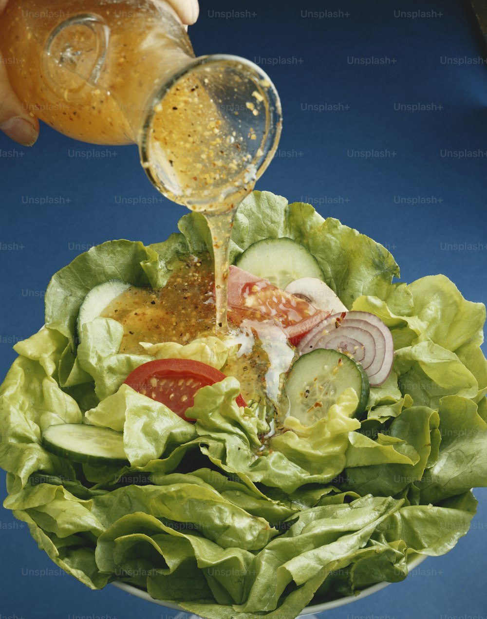 a person pouring dressing into a salad in a bowl