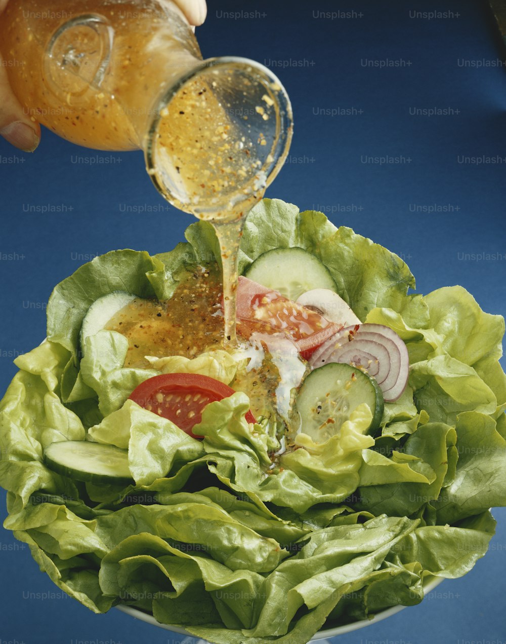 une personne versant de la vinaigrette dans une salade dans un bol