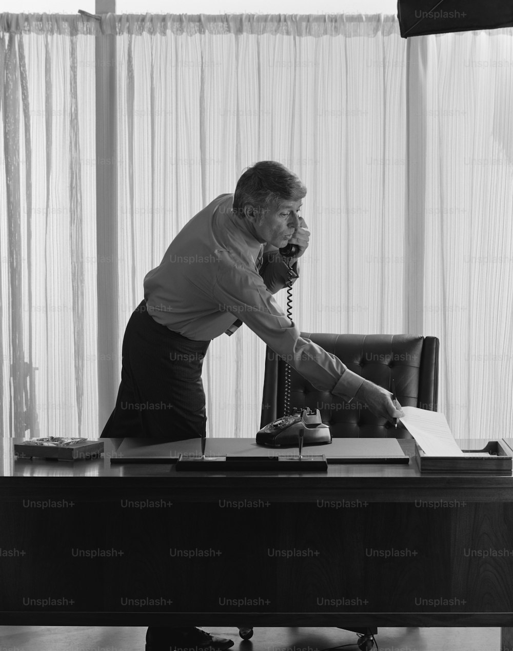 Un hombre inclinado sobre un escritorio hablando por teléfono