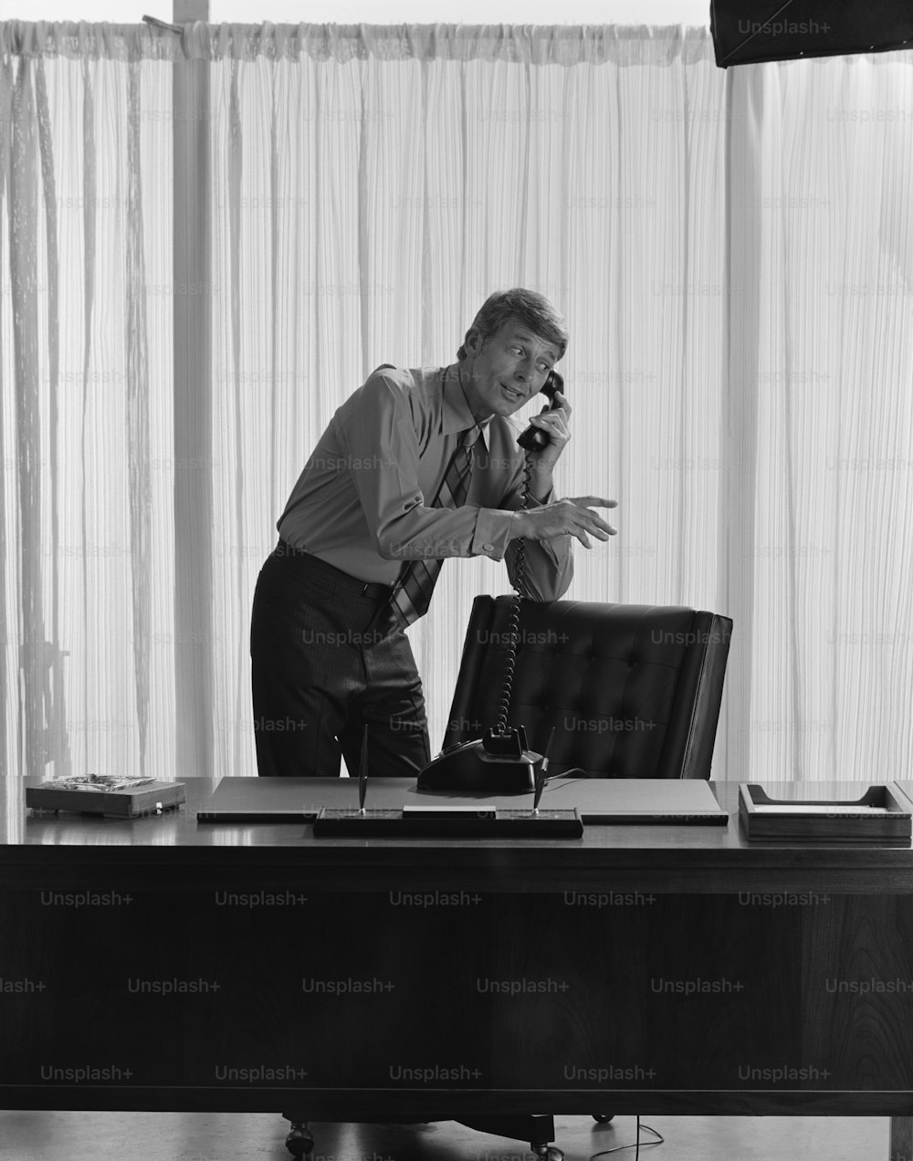 a man standing in front of a desk talking on a phone