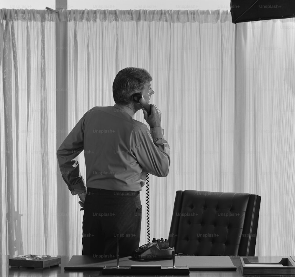 um homem parado em frente a uma mesa falando ao telefone