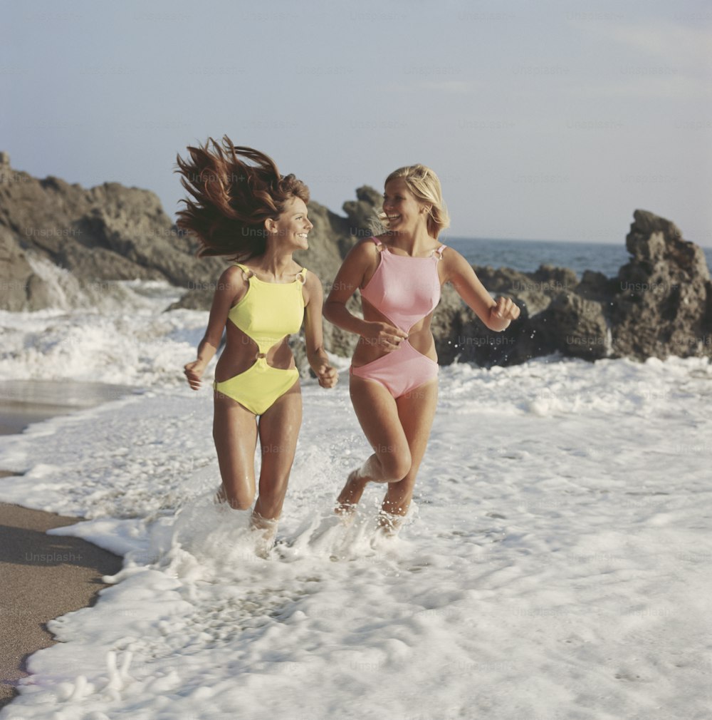 two women in bathing suits running in the ocean