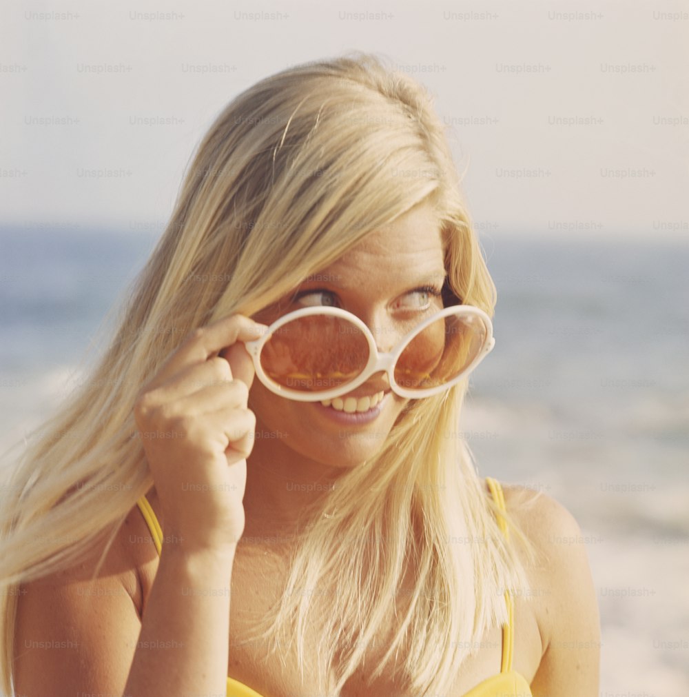 a woman in a yellow top holding up a pair of round sunglasses