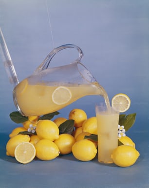 a pitcher of lemonade being poured over a pile of lemons