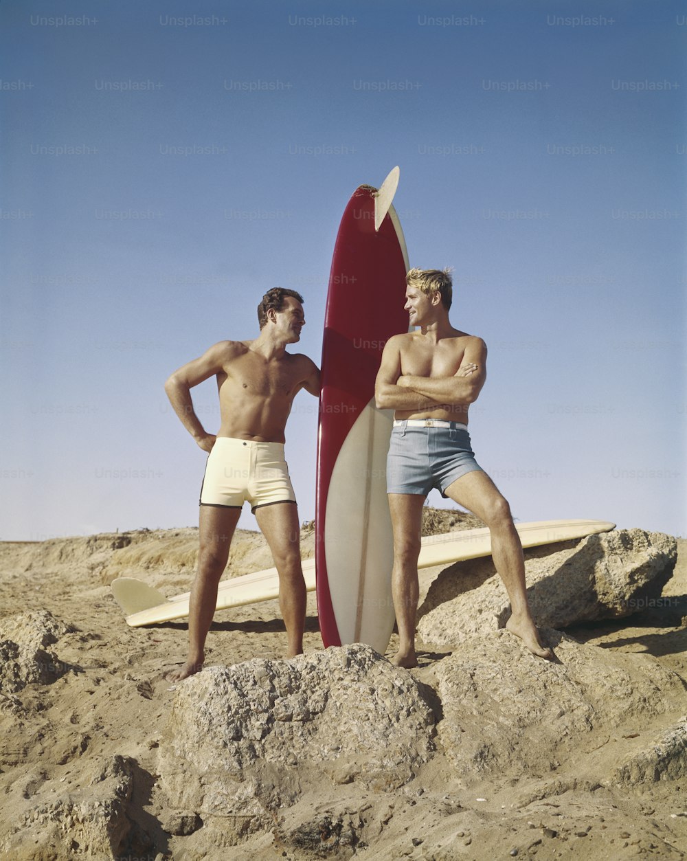 a couple of men standing next to a surfboard