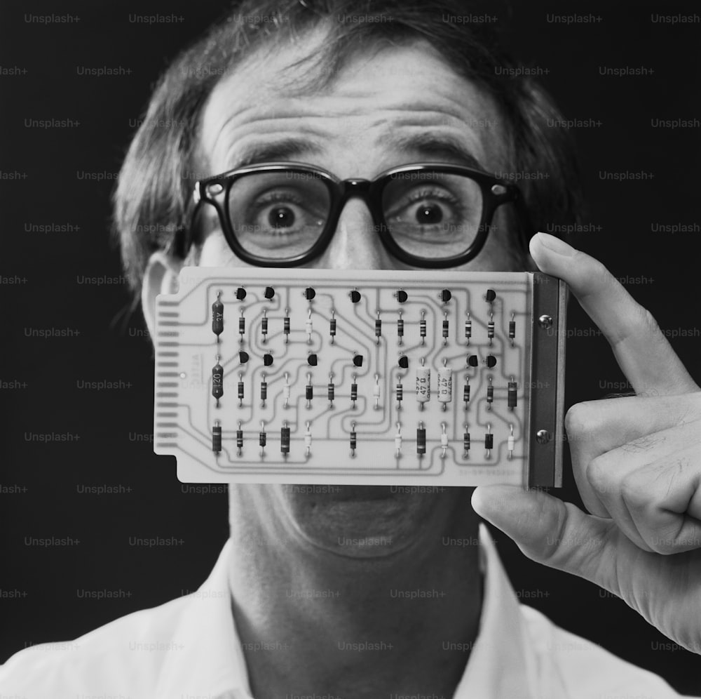 a man wearing glasses holding up a circuit board