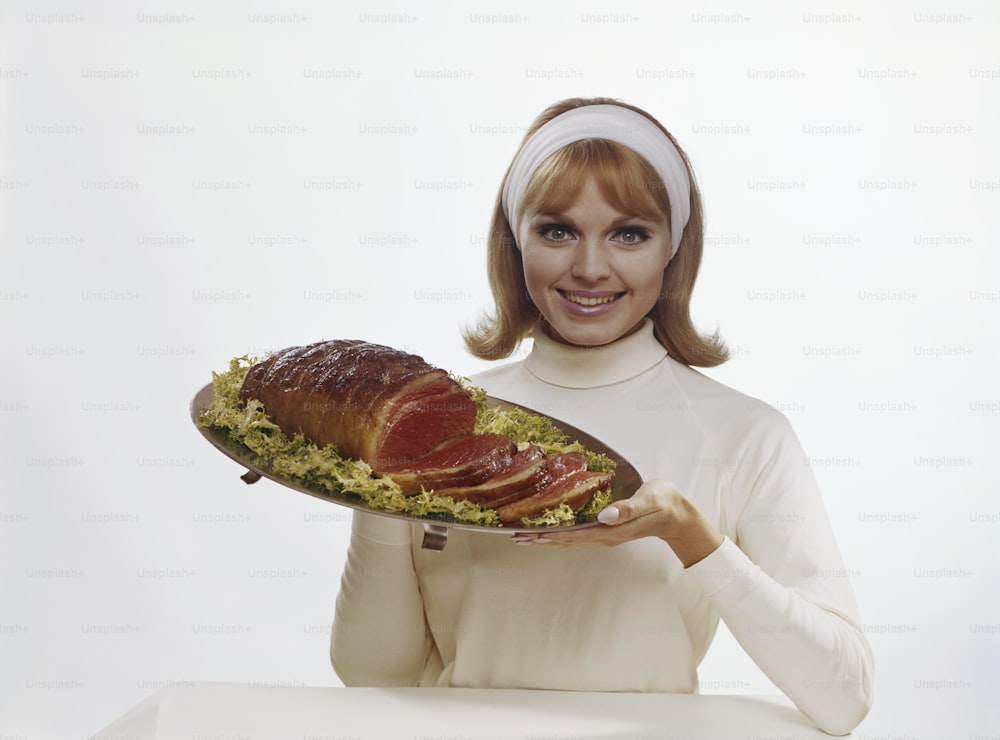 uma mulher segurando uma bandeja de carne e legumes