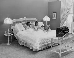 a black and white photo of two women and a child on a bed