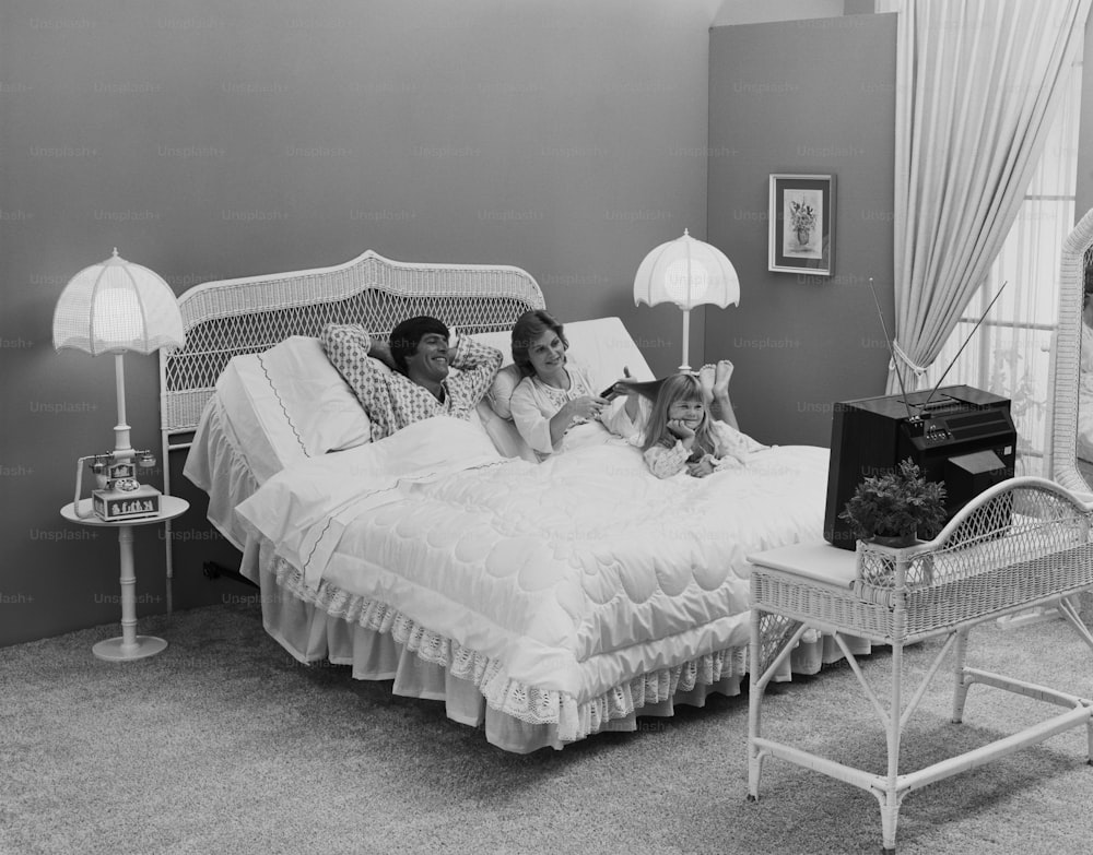a black and white photo of two women and a child on a bed