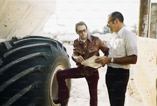 a couple of men standing next to a large tire
