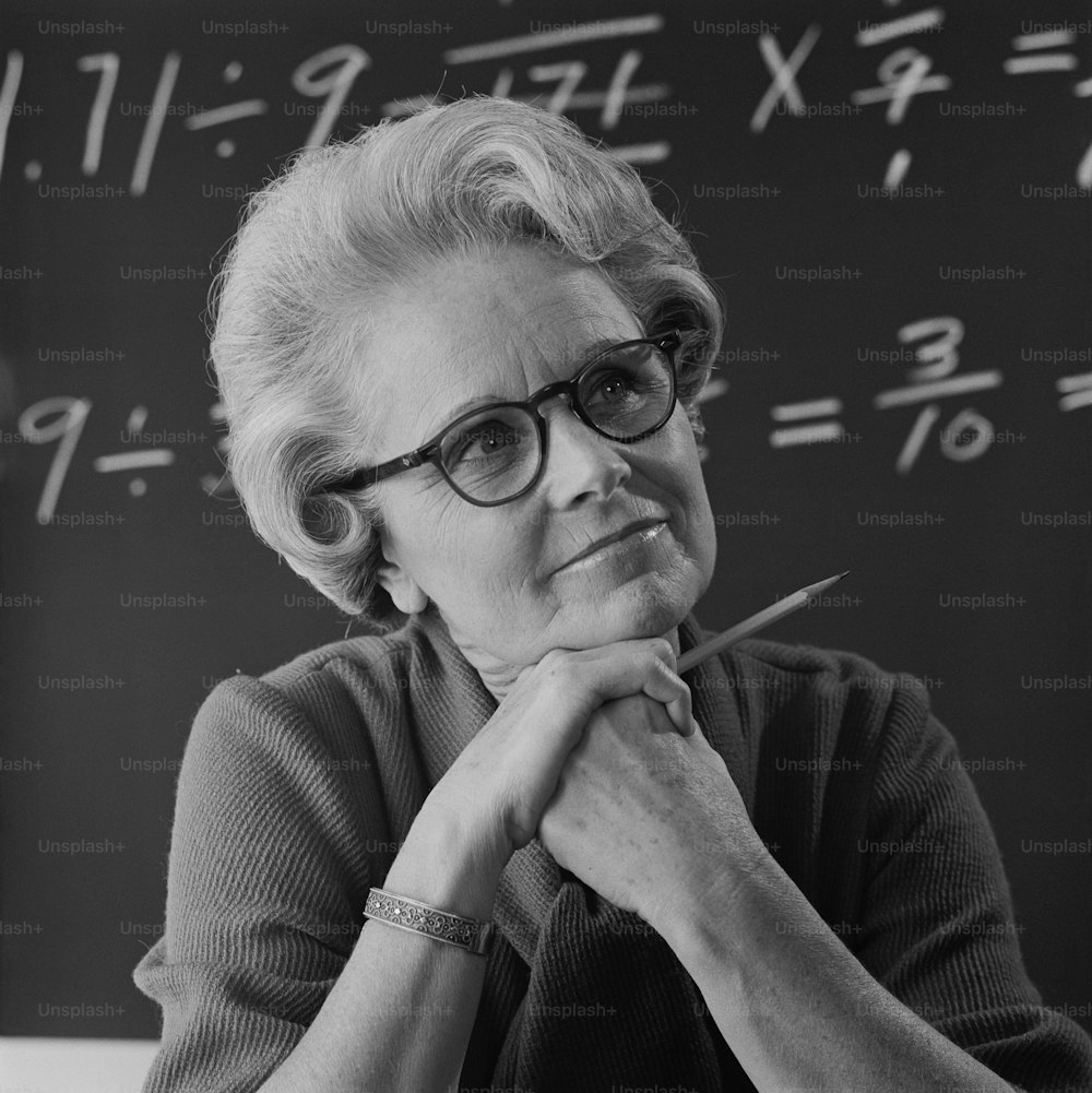 a black and white photo of a woman in front of a chalkboard