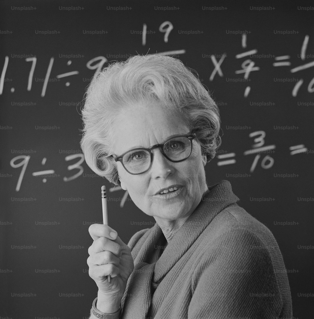 a woman holding a pencil in front of a blackboard