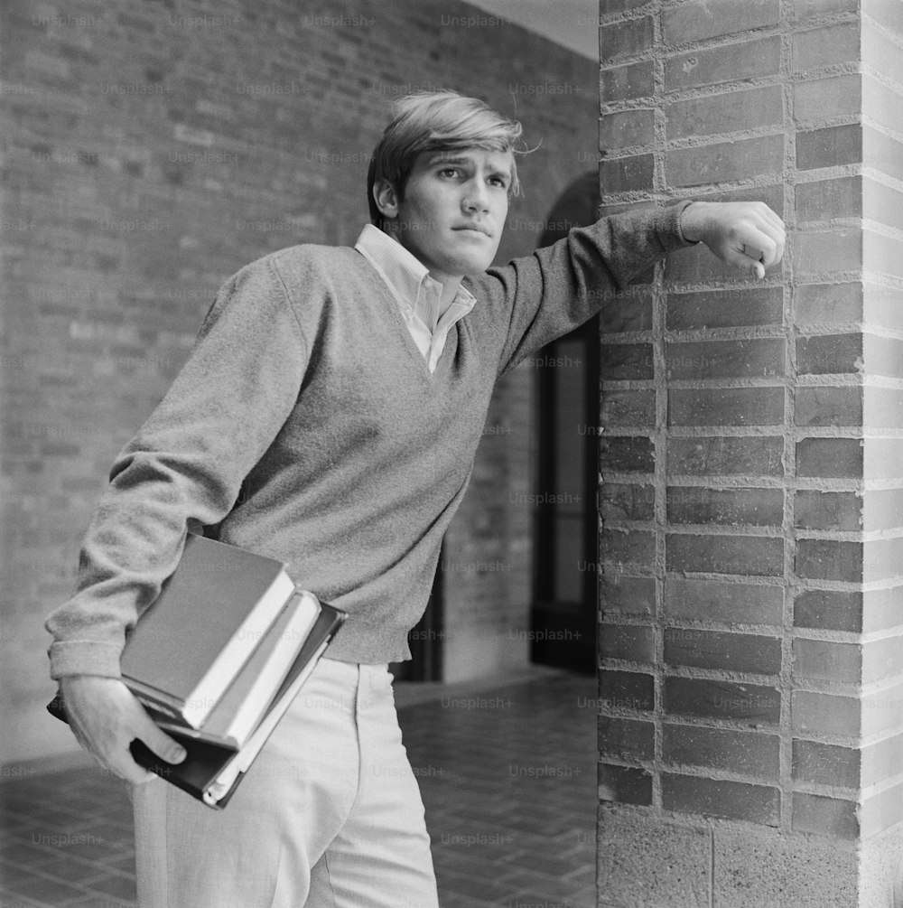 a black and white photo of a man leaning against a brick wall