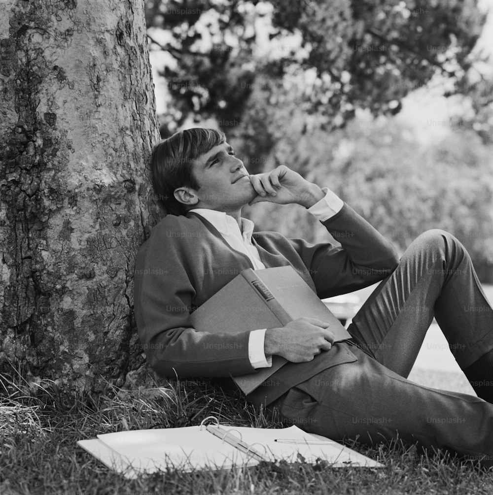 a man sitting on the ground next to a tree