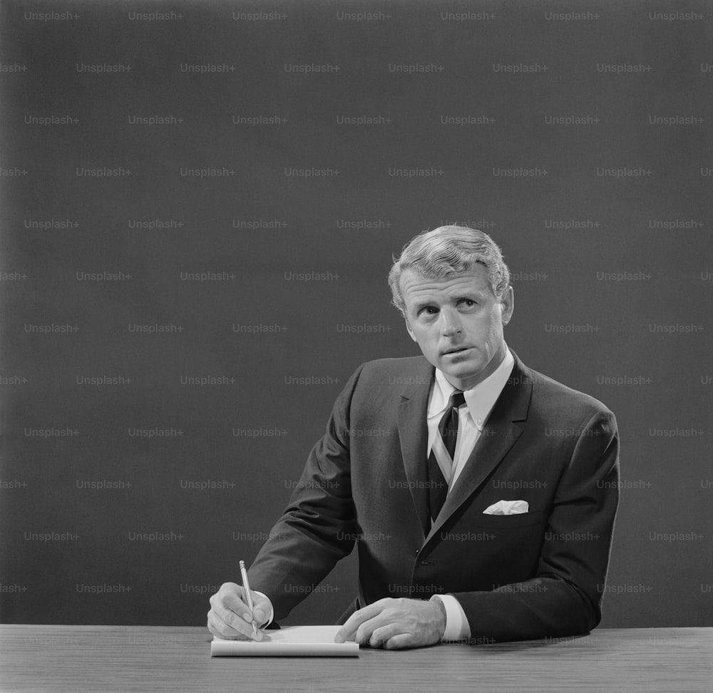 a black and white photo of a man in a suit writing