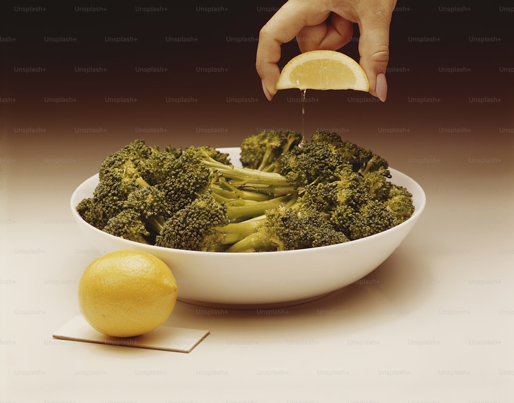 a person dipping a lemon into a bowl of broccoli
